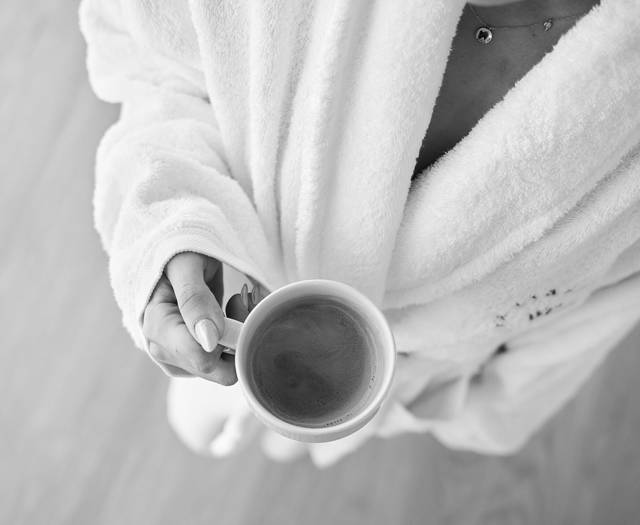 Ethereal White Resort Heraklion guest wearing the hotel's bathrobe and holding a cup of coffee